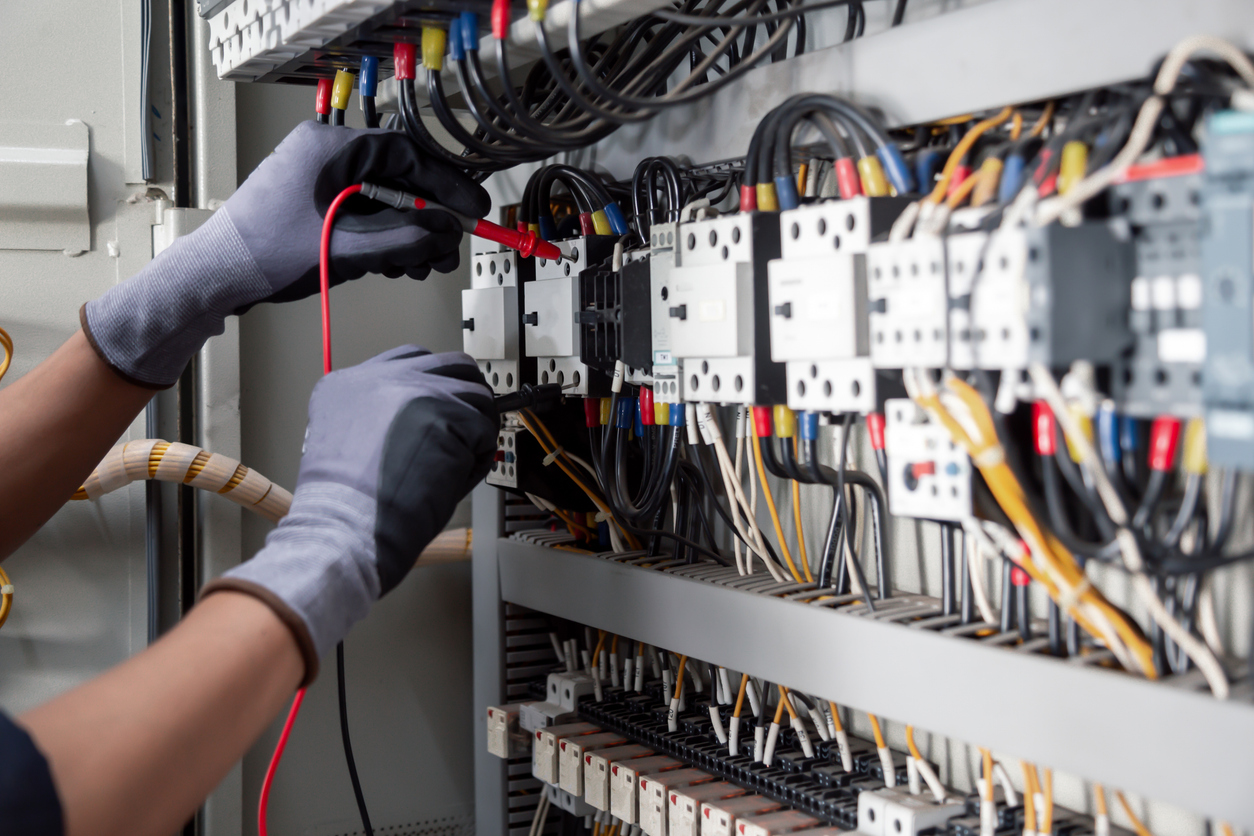 Gloved hands wiring and testing the internals of a control panel